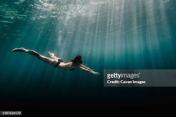 full length of woman swimming underwater in the ocean - profundo fotografías e imágenes de stock