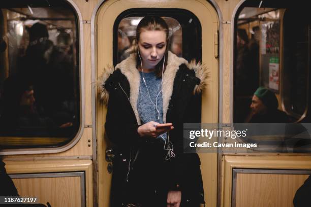 young woman listening music on phone while traveling in subway train - parka stock pictures, royalty-free photos & images