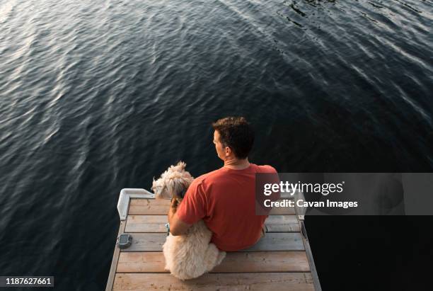 overhead view of a man and his pet dog sitting on a dock on a lake. - soft coated wheaten terrier bildbanksfoton och bilder