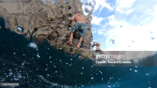 young man and woman climb up seaside cliff - cliff jumping stock pictures, royalty-free photos & images