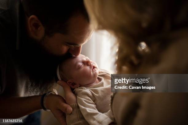 father kissing sleeping newborn daughters head in mother's arms - mum dad and baby fotografías e imágenes de stock