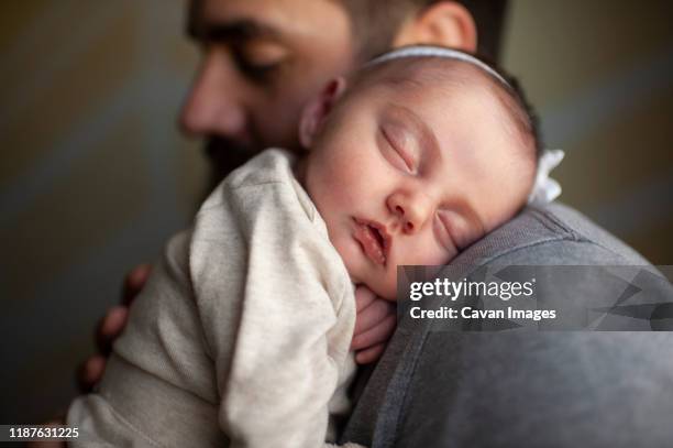 close up of newborn baby's face sleeping on father's shoulder at home - genderblend stock-fotos und bilder