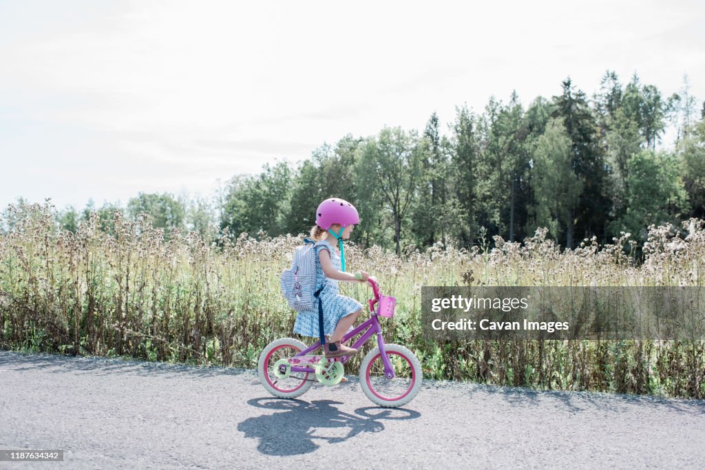 Young girl cycling home from school along a country lane in summer