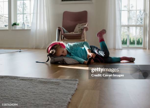 young girl laying down listening to music with headphones on at home - laminat stock-fotos und bilder