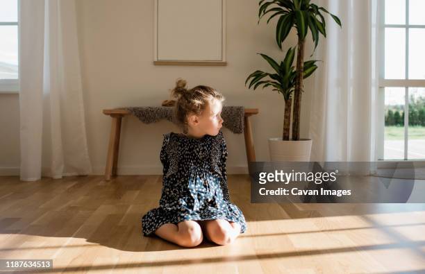 portrait of a young girl sitting alone at home looking out the window - wood laminate flooring stockfoto's en -beelden