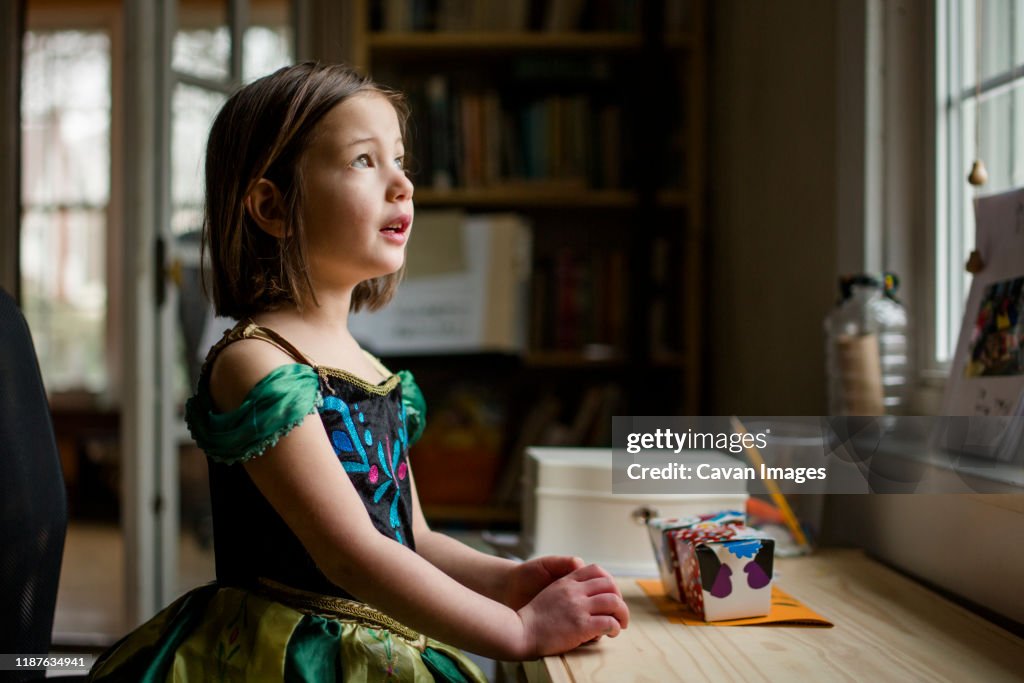 A small child plays at a window in a princess costume looking up