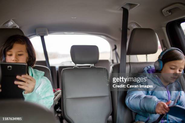 two children in the backset of a van watch tablets on a roadtrip - oh brother stock pictures, royalty-free photos & images