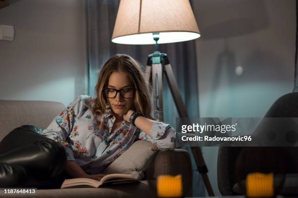 young female reading book in living room - lamp imagens e fotografias de stock
