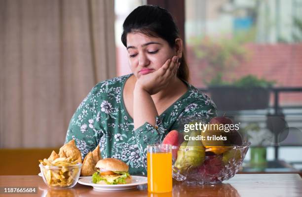 unzufriedene frau mit ungesundem und gesundem essen auf dem tisch - fat woman stock-fotos und bilder