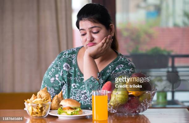 donna scontenta con cibo malsano e sano sul tavolo - fat foto e immagini stock
