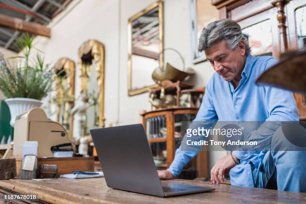 Mature man looking at computer in his antique shop