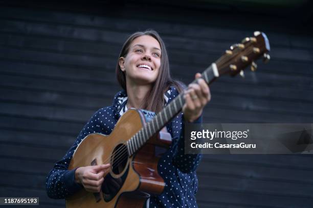 happy young female musician playing on her acoustic guitar outdoors - stock photo - songwriter stock pictures, royalty-free photos & images