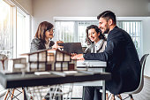 Side view image of young happy family sitting in consulting office, making property purchase. Mature female Real Estate Agent helping business couple do financial investment. Installment payment, mortgage, loan for estate concept