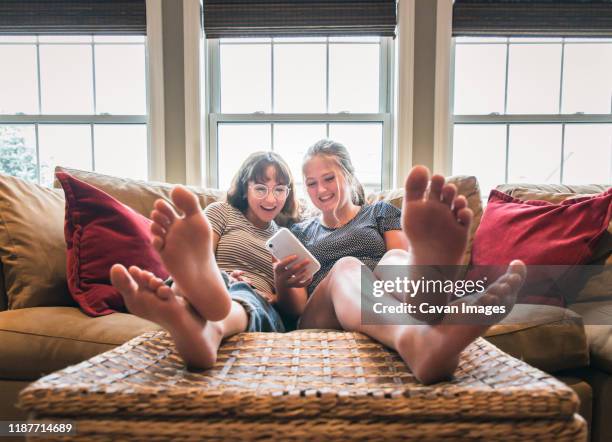 two teenage girls sitting on couch with feet up looking at cellphone. - girl soles stock pictures, royalty-free photos & images