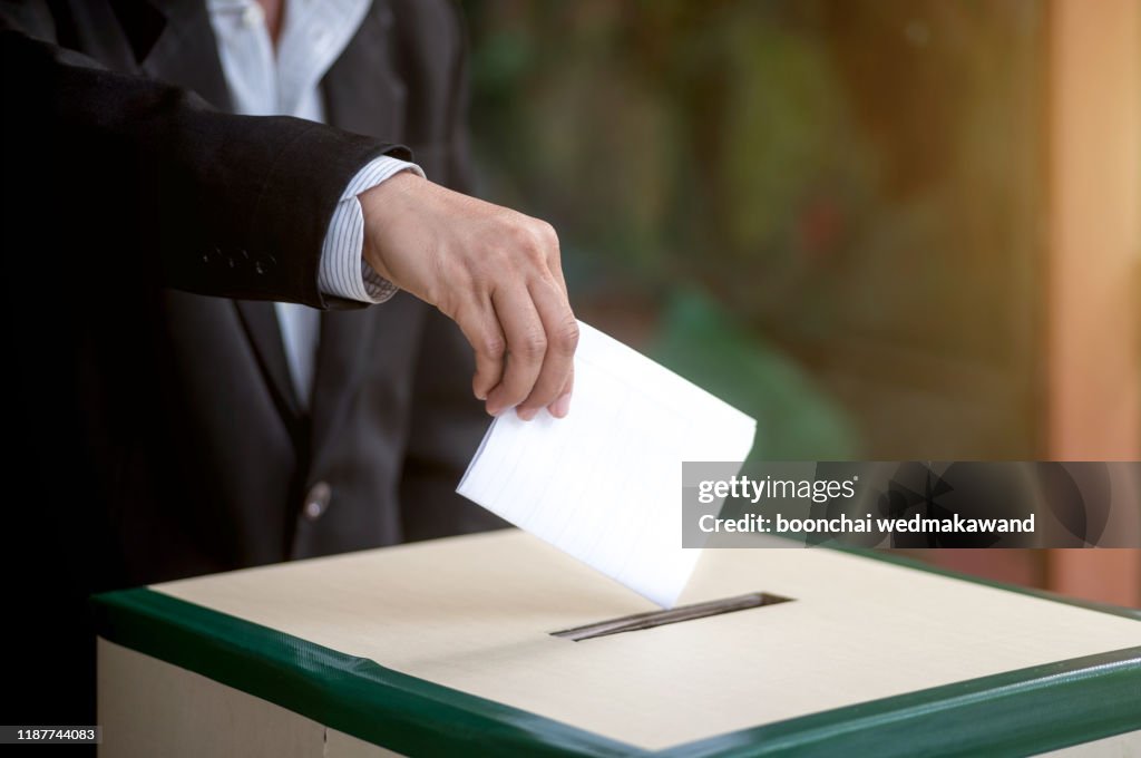 Hand of a person casting a vote into the ballot box during elections