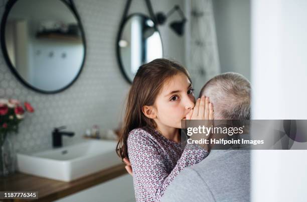 senior grandfather and granddaughter sitting indoors in bathroom, whispering in ear. - child whispering stockfoto's en -beelden