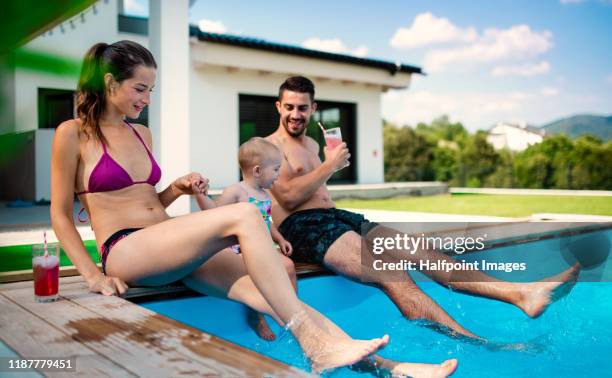 portrait of young couple with toddler girl sitting by swimming pool outdoors at home. - zwembroek stockfoto's en -beelden