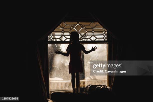 profile of little girl standing at lead paned window at sunset - little black dress stock-fotos und bilder