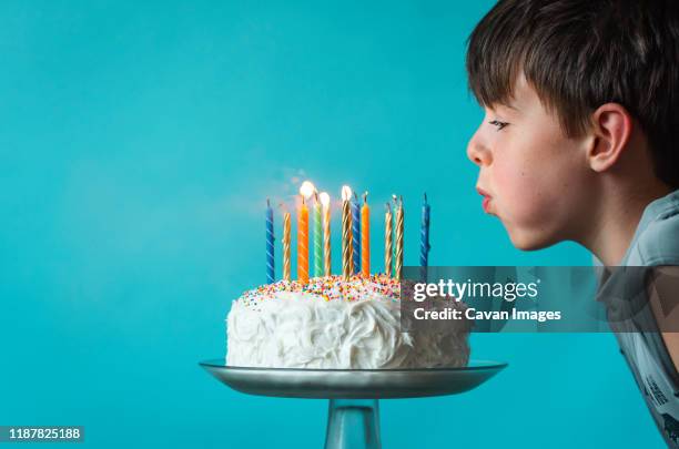 boy blowing out candles on a birthday cake against blue background. - soffiare foto e immagini stock