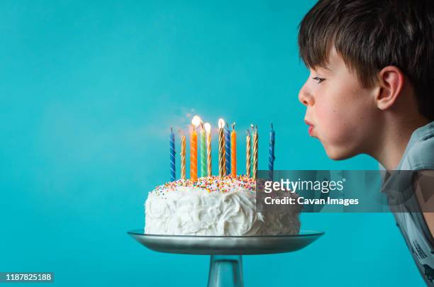 boy blowing out candles on a birthday cake against blue background. - birthday cake stock pictures, royalty-free photos & images