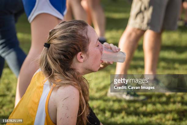 exhausted teen girl cross country runner drinks water after race - exhausted at finish line stock pictures, royalty-free photos & images