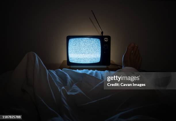 one person watches noise in tv in his bed with one foot sticking of the sheets - kommunikationskanäle stock-fotos und bilder