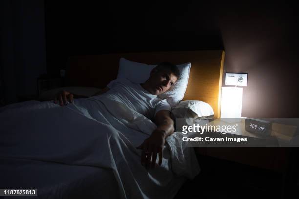 a man with insomnia looks at the clock at dawn from the bed with concern - distraught photos et images de collection