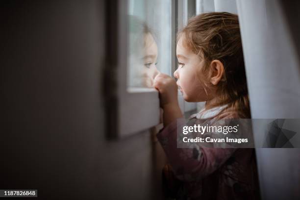 side view of young girl looking outside window at rain - girl shower stock-fotos und bilder