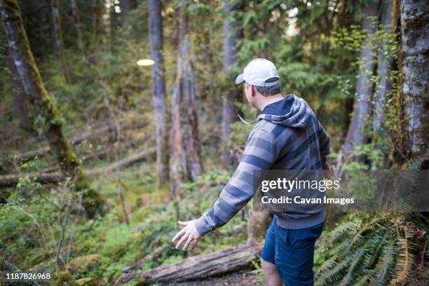 man throws frisbee in forest during a disk golf game. - frisbee golf stock pictures, royalty-free photos & images