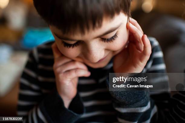 boy 7-8 years old with long eyelashes looking down with hands by face - fingers in ears stock pictures, royalty-free photos & images