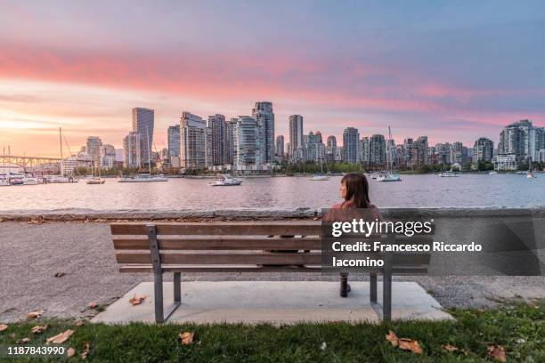 woman sitting on a bench looking at vancouver skyline, sunset from from the island park walk. british columbia, canada - カナダ バンクーバー ストックフォトと画像