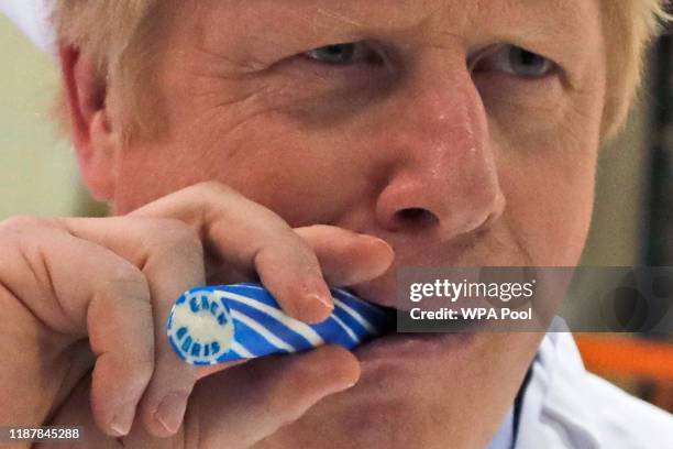 Britain's Prime Minister Boris Johnson eats a candy stick which reads "Back Boris" during a General Election campaign trail stop at Coronation Candy...