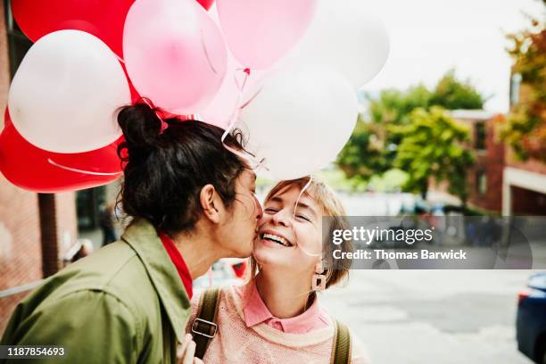 man kissing smiling girlfriend on cheek while giving her balloons during date - バレンタイン　友人 ストックフォトと画像