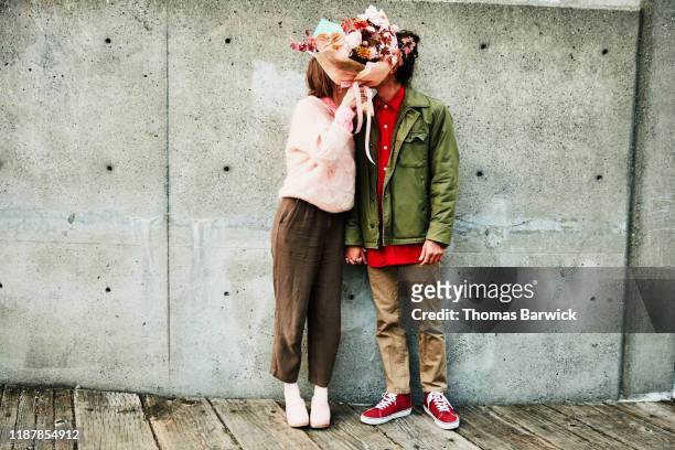 portrait of couple kissing while hidden behind bouquet of flowers - couple photos et images de collection