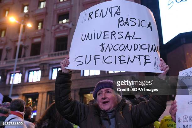 Woman holds a placard in favour of universal basic income during the protest. Hundreds of people gathered at Callao square in Madrid to mark the...