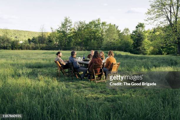 group of friends enjoying dinner in rustic field - table wine food stockfoto's en -beelden