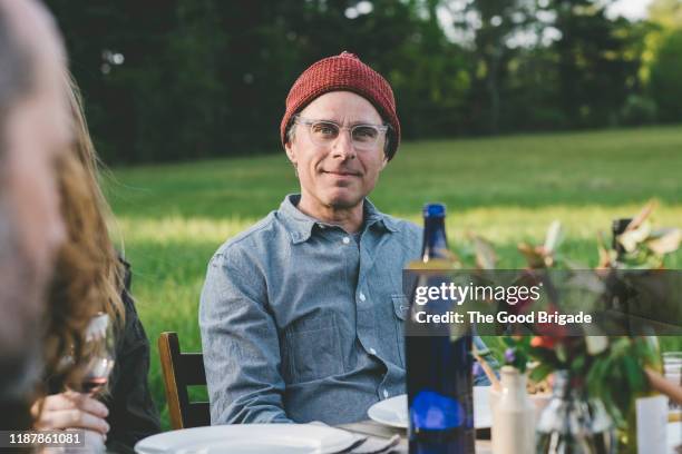 portrait of man in wool cap and glasses sitting at table in field - hipster persona stock-fotos und bilder