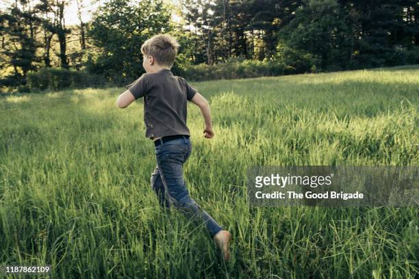 rear view of boy running  in grassy field - boy running back stock pictures, royalty-free photos & images