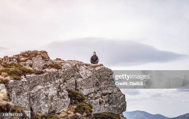 young man meditating on a mountain top. - wide angle lens stock pictures, royalty-free photos & images