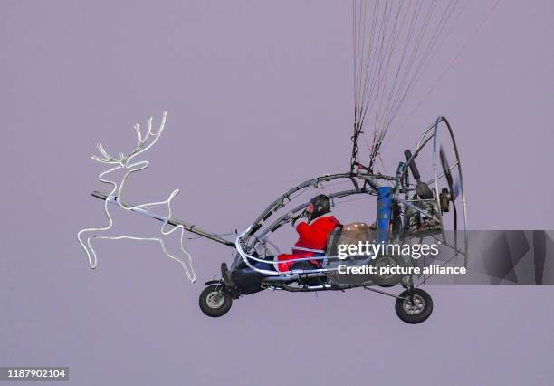 December 2019, Brandenburg, Frankfurt : In a trike with a motor paraglider, a man in a Santa Claus costume and illuminated reindeer flies over the...