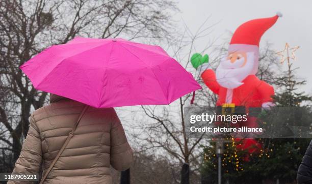 December 2019, Lower Saxony, Hanover: A woman walks past an inflatable Santa Claus with an umbrella. Photo: Julian Stratenschulte/dpa