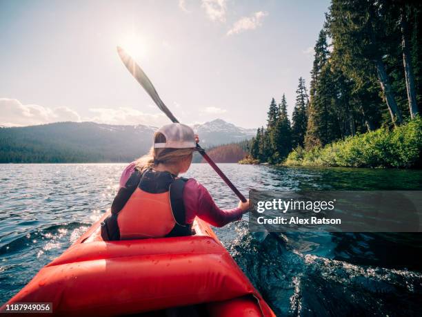 a female pack-rafter paddles across the mountainous callaghan lake near whistler, bc - canoe ストックフォトと画像