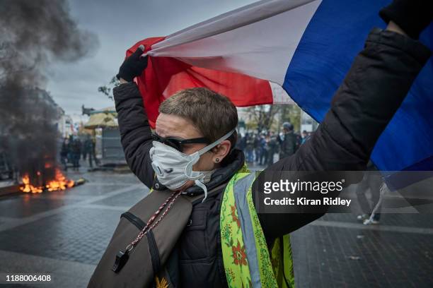 Gilet Jaune, or Yellow Vest, protestor holds a French Tricolor as protests to mark the Anniversary of the Gilets Jaune movement turn violent at Place...
