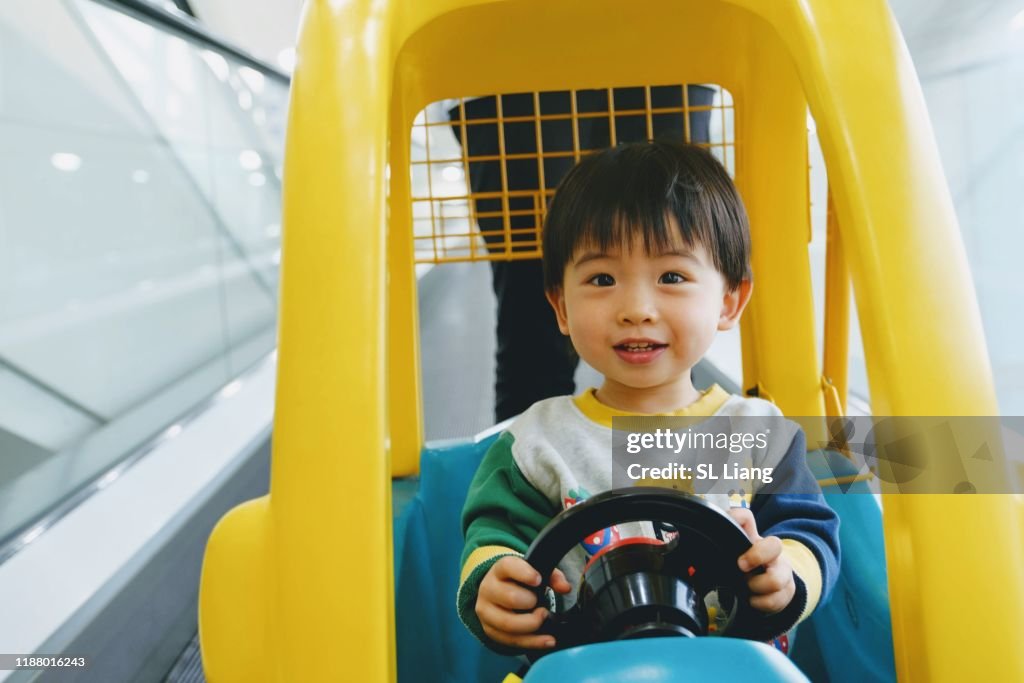 Toddler boy riding tricycle on car in supermaket