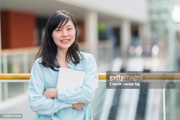 portrait of female university student while holding textbook - beautiful college girls stock pictures, royalty-free photos & images