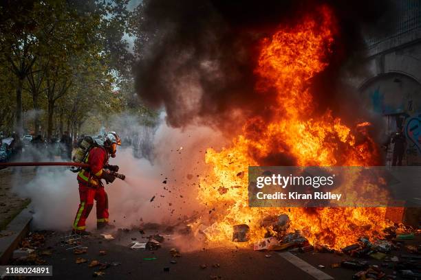 French fireman extinguishes a burning barricade as protests to mark the Anniversary of the Gilets Jaune movement turn violent in Paris as thousands...