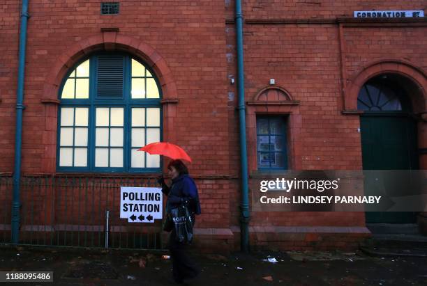 Woman shelters from the rain beneath an umbrella as she passes a sign for a polling station on Coronation Street in Salford, northern England, as...