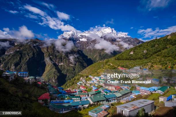 Panoramic aerial view over the town, mountainous landscape and snow-covered peak of Mt. Kongde Ri in the distance.