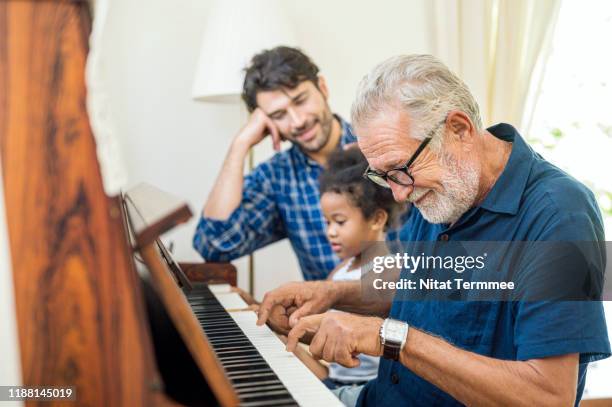 family spend time happy together. grandfather playing piano with his granddaughter and son together in living room at home. - child playing in room stockfoto's en -beelden