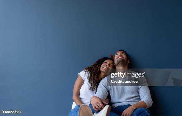 thoughtful couple at home leaning against a wall and smiling - living new house stock pictures, royalty-free photos & images